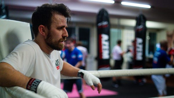 Boxtrainer lehnt nachdenklich an den Seilen im Boxstudio