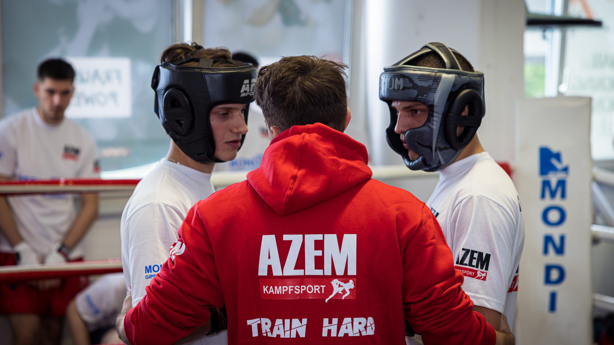 Trainer spricht mit zwei jungen Kämpfern im Helm vor dem Sparring