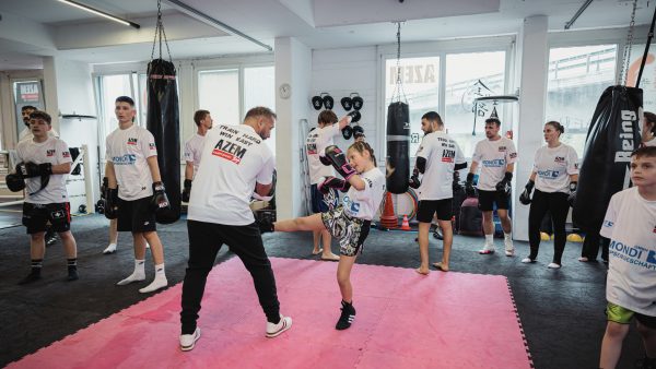 Junges Mädchen tritt im Kampfsporttraining bei AZEM gegen einen Trainer, umgeben von weiteren Teilnehmern