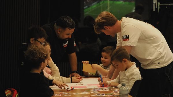 Kinder basteln und malen gemeinsam an einem Tisch, betreut von zwei AZEM Coaches in Schwarz und Weiss