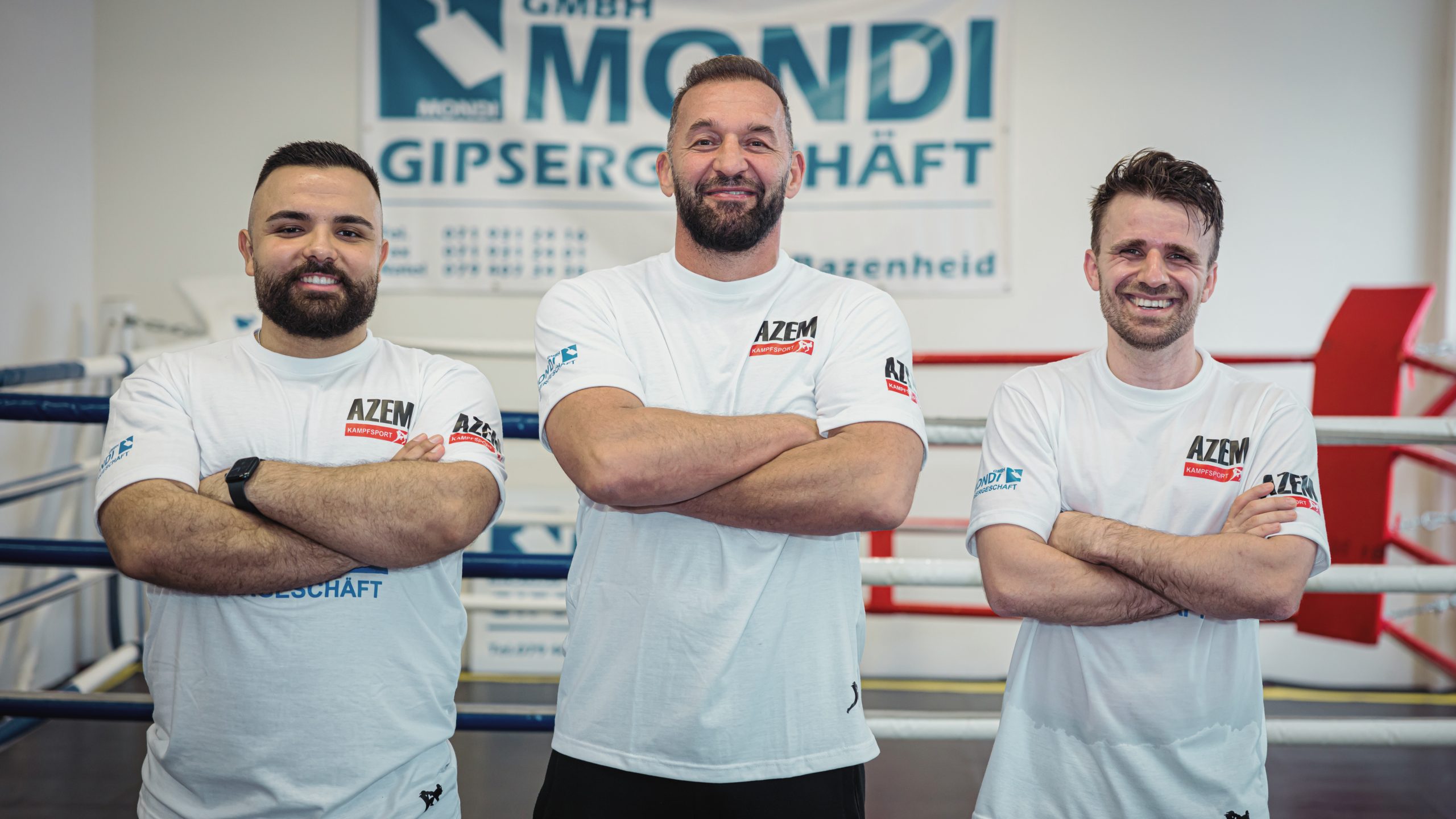 Drei AZEM Kampfsporttrainer stehen mit verschränkten Armen im Boxring und lächeln in die Kamera