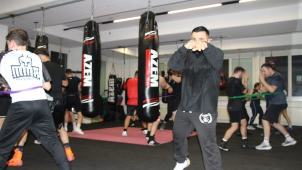 Trainer mit Fokus nach vorne in Boxhaltung zwischen Sandsäcken.