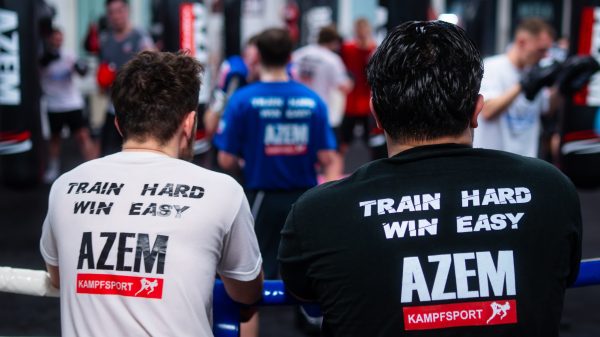 Zwei Sportler beobachten Training im AZEM Gym von hinten.