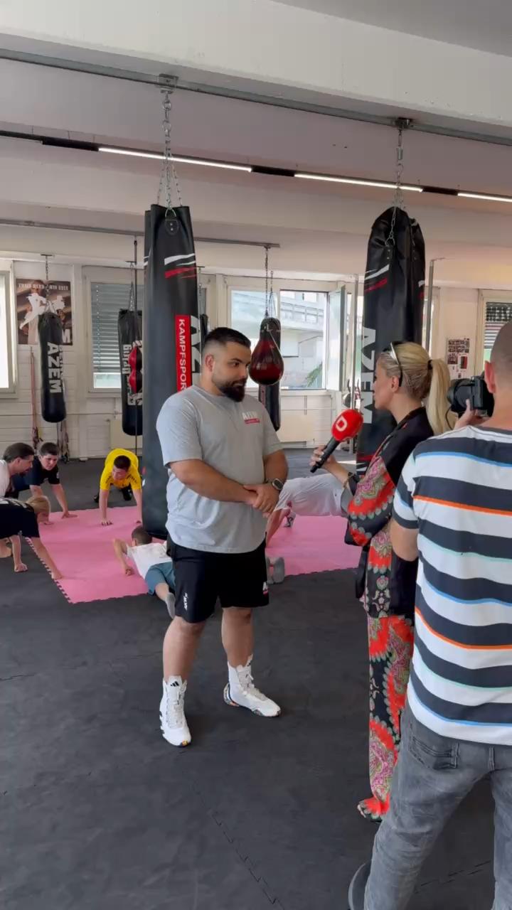 Trainer von AZEM Kampfsport gibt ein TV-Interview während Kinder auf der Matte trainieren